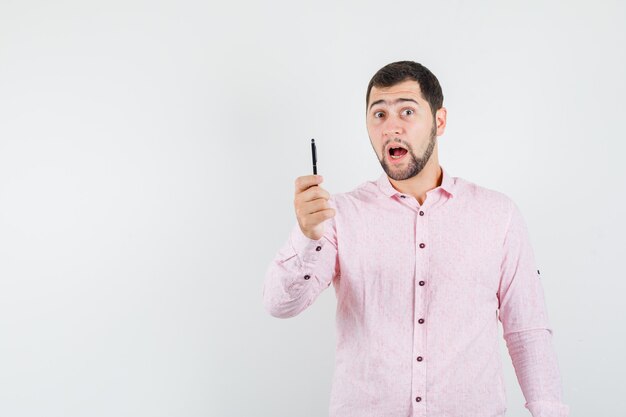 Jovem segurando uma caneta em uma camisa rosa e parecendo surpreso