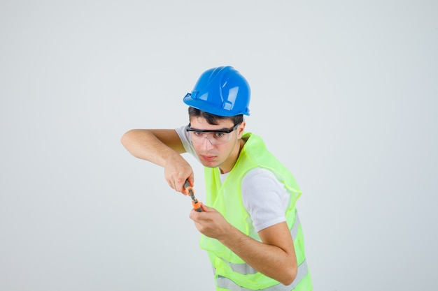 Jovem segurando uma pinça em uniforme de construção e olhando focado.