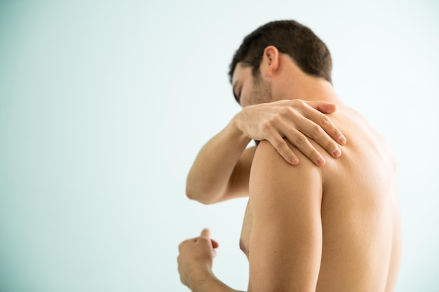 Jovem sem camisa sofrendo de dor muscular no ombro e visitando um spa para aliviá-lo