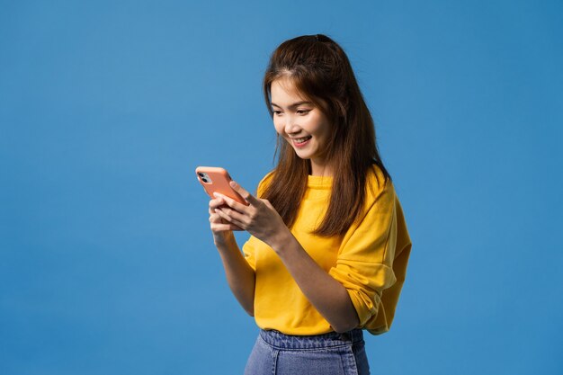 Jovem senhora asiática usando telefone com expressão positiva, sorri amplamente, vestida com roupas casuais, sentindo felicidade e estando isolada sobre fundo azul. Mulher feliz adorável feliz alegra sucesso.