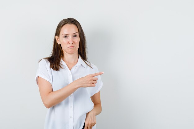 Jovem senhora com blusa branca apontando para o lado