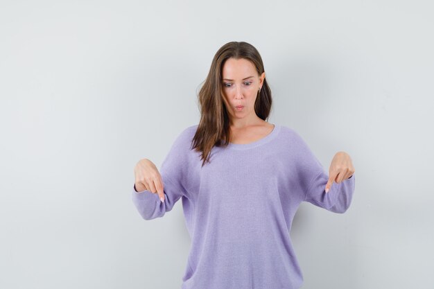 Jovem senhora com camisa casual apontando para baixo e parecendo surpresa