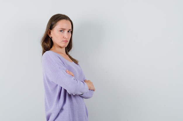 Jovem senhora com camisa casual em pé com os braços cruzados e parecendo triste