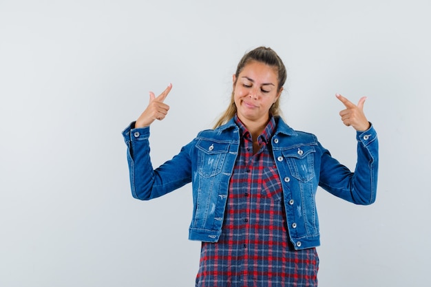 Jovem senhora com camisa, jaqueta, apontando para si mesma e orgulhosa, vista frontal.