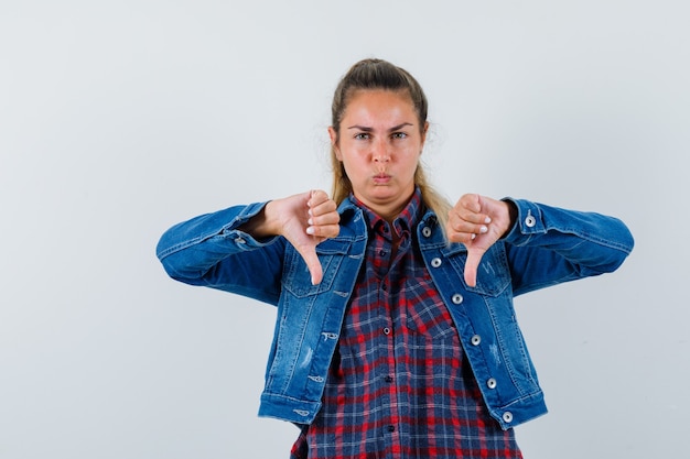 Foto grátis jovem senhora com camisa, jaqueta mostrando dois polegares para baixo e parecendo sombria, vista frontal.