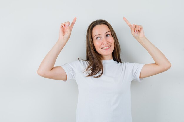 Jovem senhora com camiseta branca apontando para cima e parecendo alegre