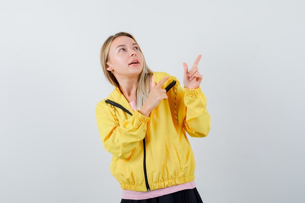 Jovem senhora com camiseta, jaqueta apontando para o canto superior direito e parecendo confiante