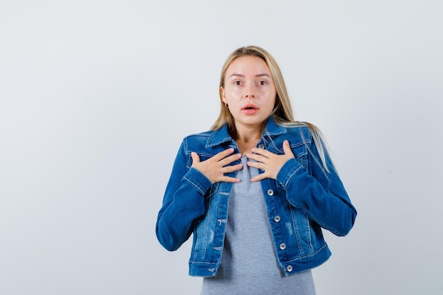 Jovem senhora com camiseta, jaqueta jeans, saia segurando as mãos no peito e parecendo indefesa