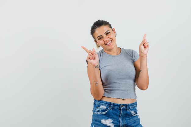 Jovem senhora com camiseta, shorts apontando para cima e parecendo alegre