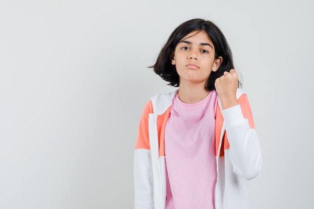 Jovem senhora com casaco, camisa rosa mostrando o punho e parecendo poderosa