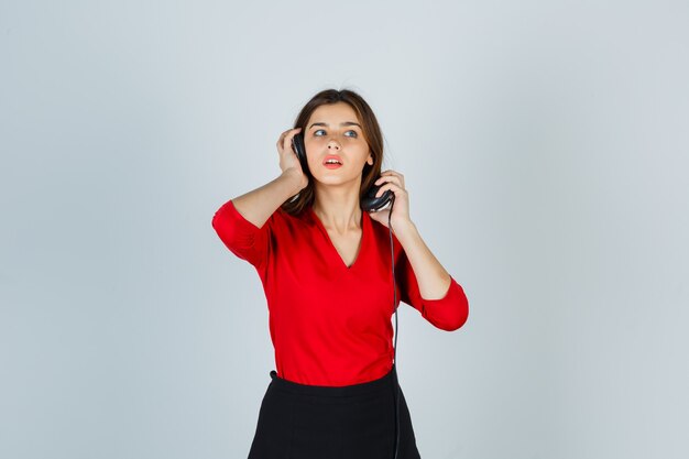 Jovem senhora com fones de ouvido na blusa vermelha, saia posando em pé e bonita