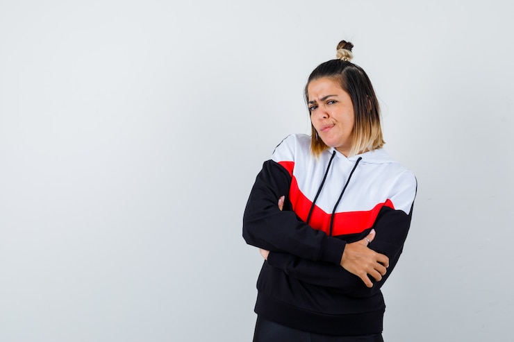Foto grátis jovem senhora com suéter com capuz em pé com os braços cruzados e parecendo séria