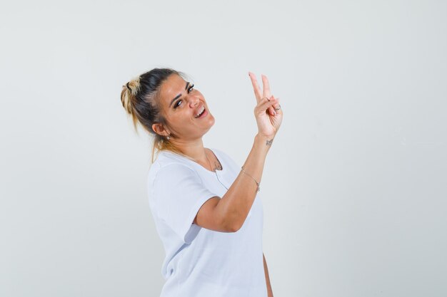 Jovem senhora com uma camiseta mostrando o sinal V e parecendo confiante