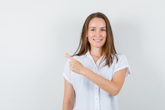 Jovem senhora de blusa branca apontando para a direita e parecendo feliz