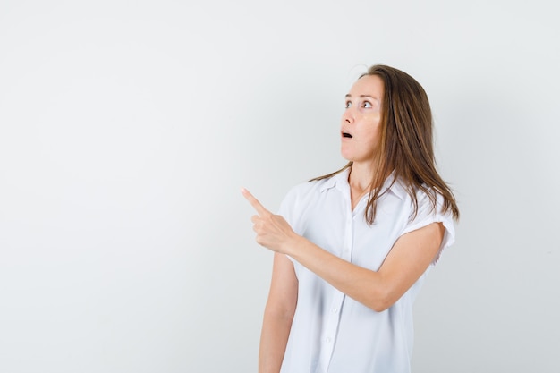 Jovem senhora de blusa branca apontando para o lado e parecendo curiosa