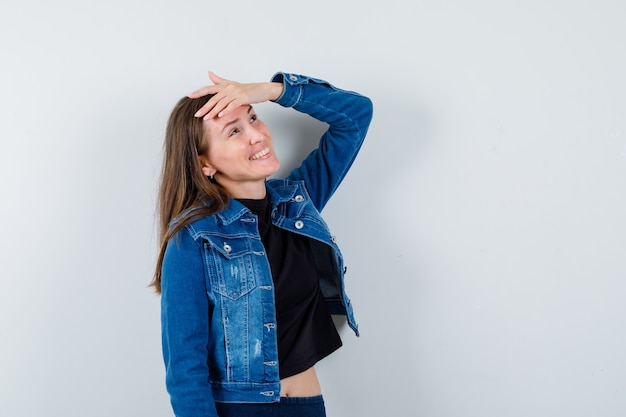 Jovem senhora de blusa, jaqueta, segurando a mão na testa enquanto posava e parecia um sonho, vista frontal.