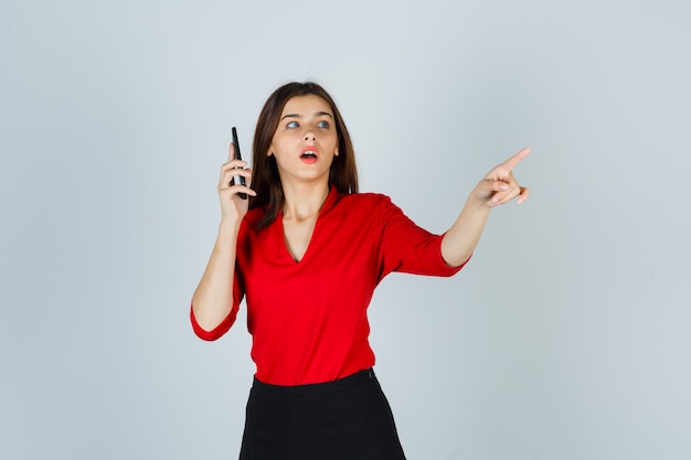 Jovem senhora de blusa vermelha, saia falando no celular enquanto aponta para o lado