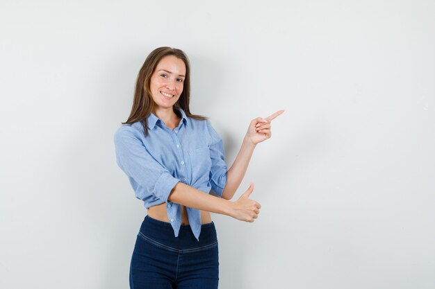 Jovem senhora de camisa azul, calça apontando para fora com o polegar para cima e parecendo alegre