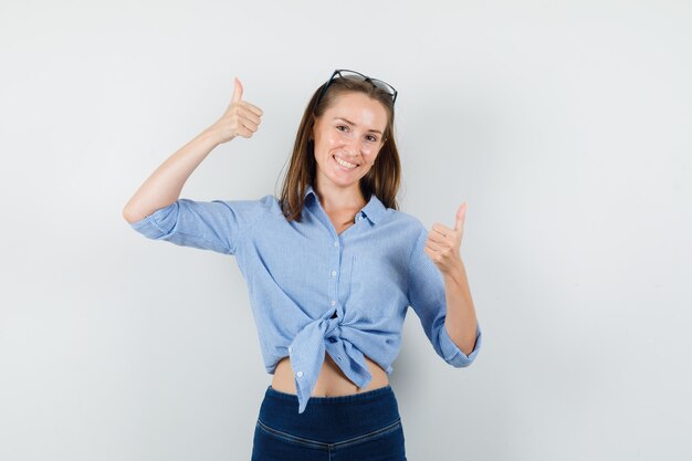 Jovem senhora de camisa azul, calça mostrando os polegares para cima e parecendo satisfeita