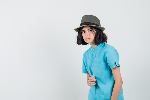 Jovem senhora de camisa azul, chapéu, olhando para o lado e parecendo animada