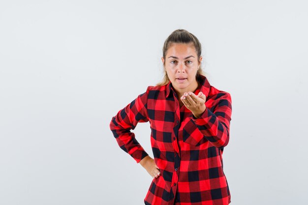 Jovem senhora de camisa casual, esticando a mão em um gesto de questionamento e parecendo perplexo, vista frontal.