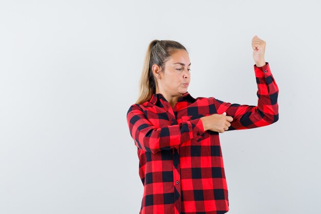 Jovem senhora de camisa casual, mostrando os músculos do braço e parecendo confiante, vista frontal.