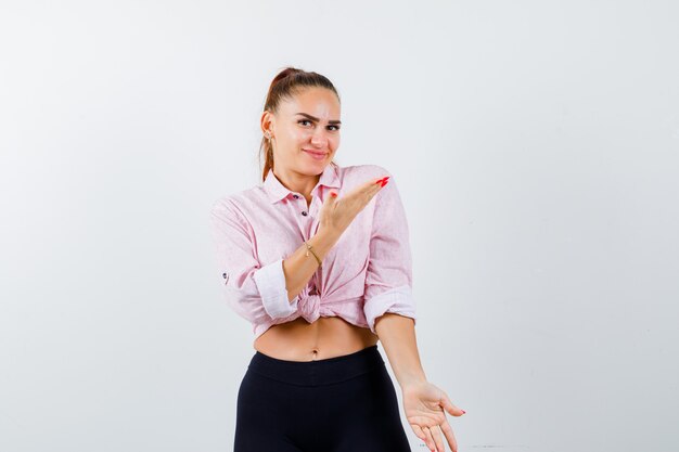 Jovem senhora de camisa fingindo mostrar algo e parecendo alegre, vista frontal.