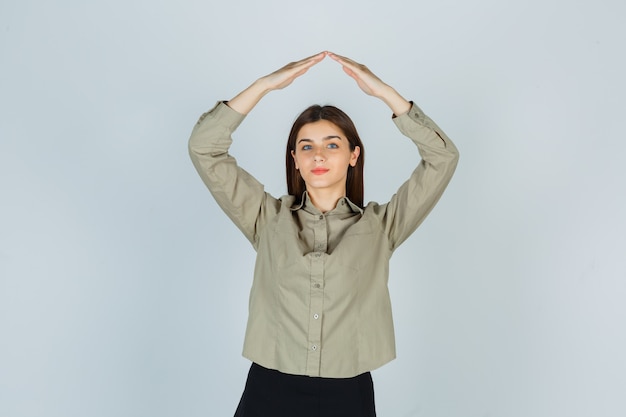 Foto grátis jovem senhora de camisa, saia mostrando gesto do telhado da casa e parecendo satisfeita