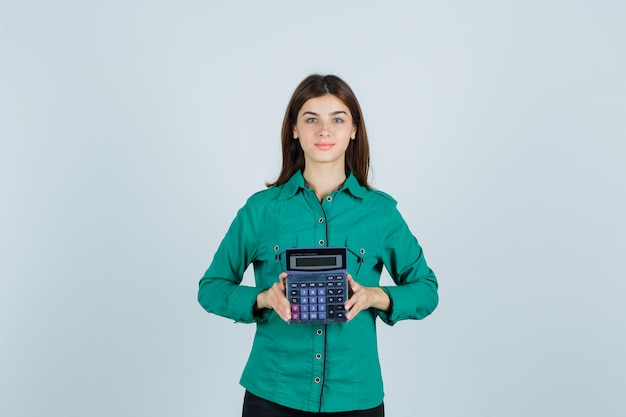 Jovem senhora de camisa verde, segurando a calculadora e parecendo confiante, vista frontal.