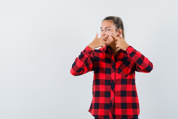 Foto grátis jovem senhora de camisa xadrez apertando a espinha na bochecha