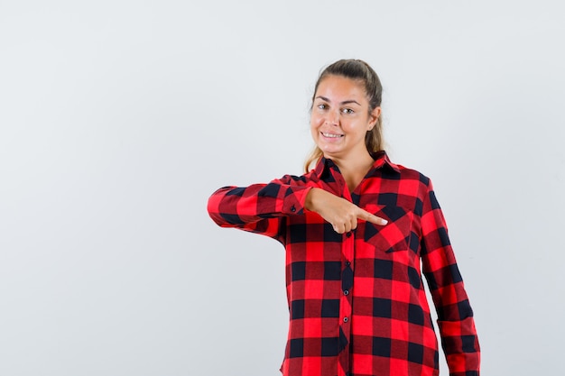 Jovem senhora de camisa xadrez apontando para baixo e parecendo alegre