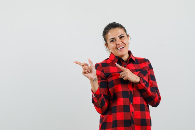 Jovem senhora de camisa xadrez apontando para o lado e parecendo alegre