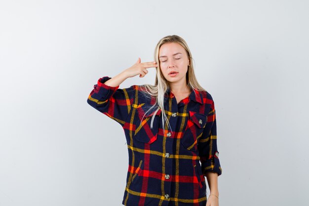 Jovem senhora de camisa xadrez, atirando em si mesma com uma arma de mão e parecendo sem esperança, vista frontal.