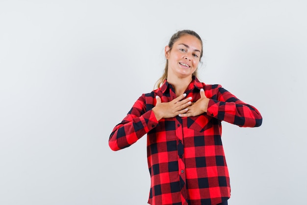 Jovem senhora de camisa xadrez de mãos dadas no peito e parecendo grata