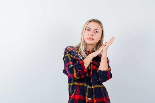 Jovem senhora de camisa xadrez, esfregando as mãos e olhando pensativa, vista frontal.