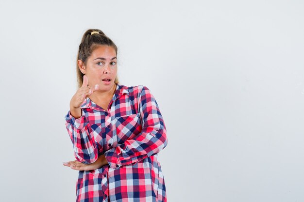 Jovem senhora de camisa xadrez, oferecendo a mão para tremer e olhando orgulhosa, vista frontal.