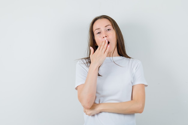 Jovem senhora de camiseta branca bocejando e parecendo com sono