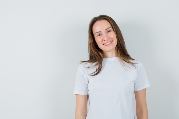 Foto grátis jovem senhora de camiseta branca olhando para a câmera e parecendo feliz