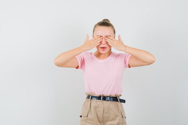 Jovem senhora de camiseta e calça cobrindo os olhos com as mãos e parecendo assustada