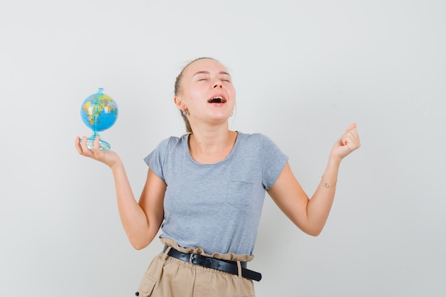 Jovem senhora de camiseta e calça segurando o globo da escola e parecendo feliz