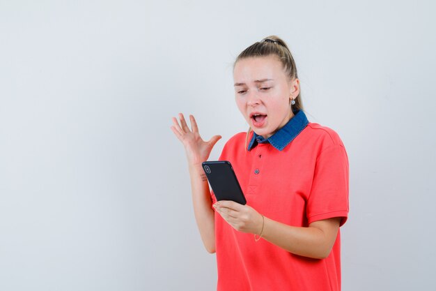 Jovem senhora de camiseta olhando para o celular e parecendo animada