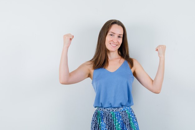 Jovem senhora de camiseta, saia mostrando gesto de vencedor e parecendo feliz