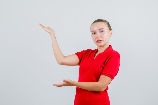 Jovem senhora de camiseta vermelha dando as boas-vindas ou mostrando algo