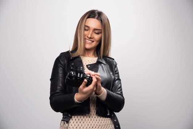 Jovem senhora de jaqueta de couro preta tirando fotos com a câmera de forma positiva e sorridente.