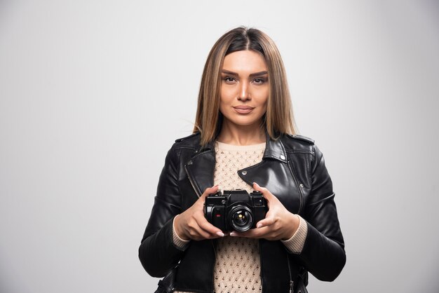 Jovem senhora de jaqueta de couro preta tirando fotos com a câmera de forma séria e profissional.