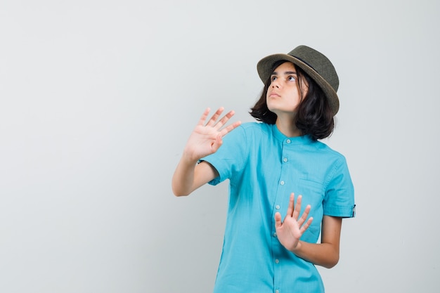 Jovem senhora defendendo com as mãos na camisa azul, chapéu