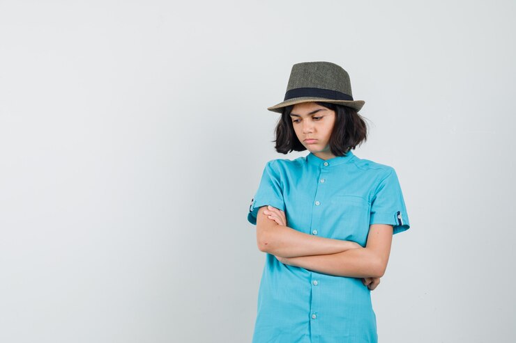 Foto grátis jovem senhora em pé com os braços cruzados, camisa azul, chapéu e aparência ofendida