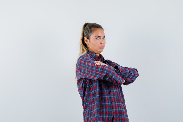 Jovem senhora em pé com os braços cruzados em uma camisa e olhando confiante, vista frontal.