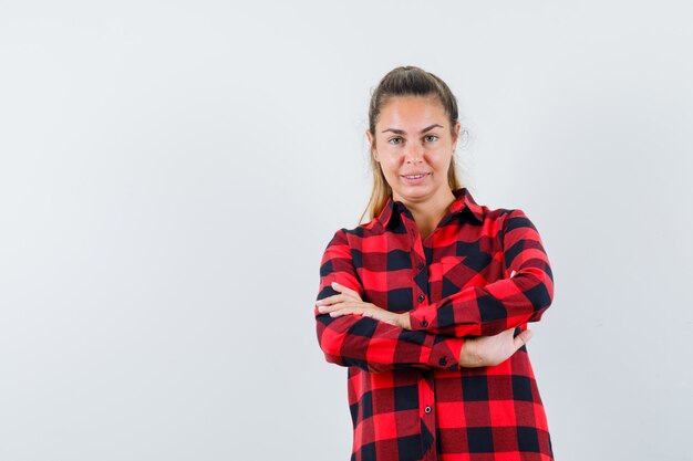 Jovem senhora em pé com os braços cruzados em uma camisa xadrez e parecendo confiante