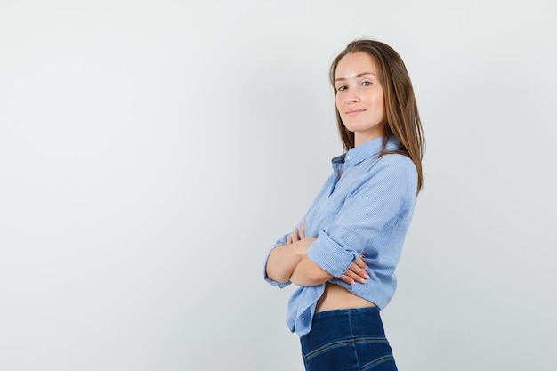 Jovem senhora em pé com os braços cruzados na camisa azul